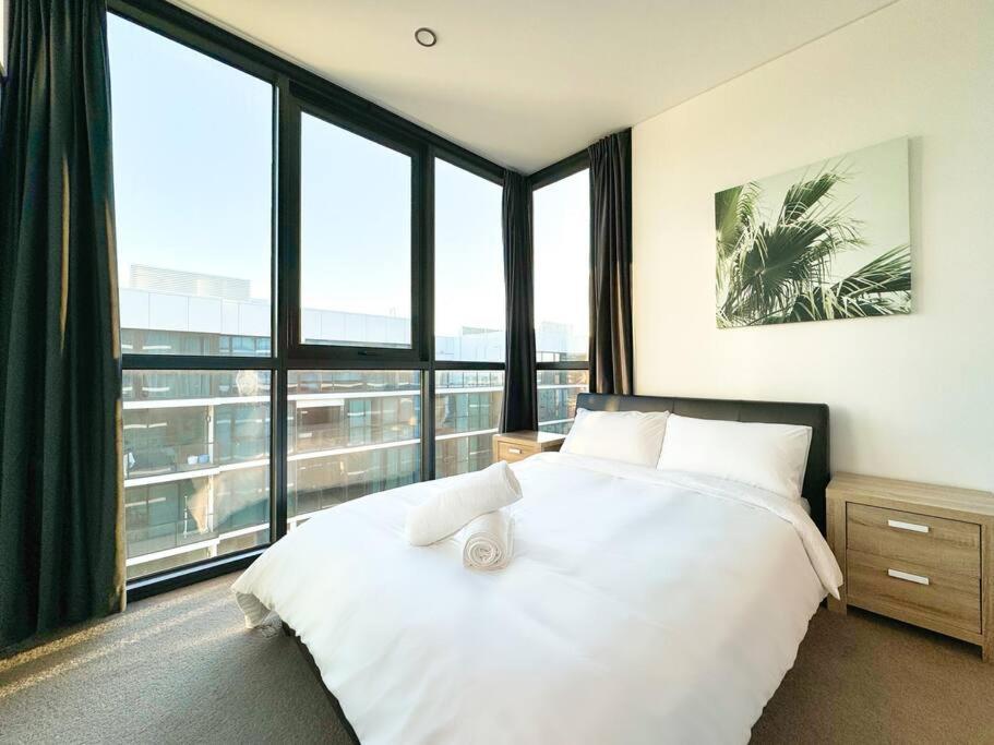 ein weißes Bett in einem Zimmer mit großen Fenstern in der Unterkunft High-Rise Heaven - West Franklin in Adelaide