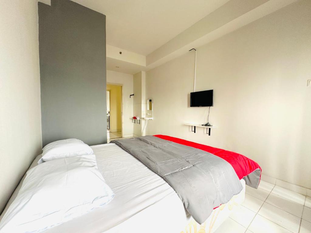 um quarto com uma cama branca e um cobertor vermelho em RedLiving Apartment @ Dramaga Tower by Liana Room em Bubulak 3