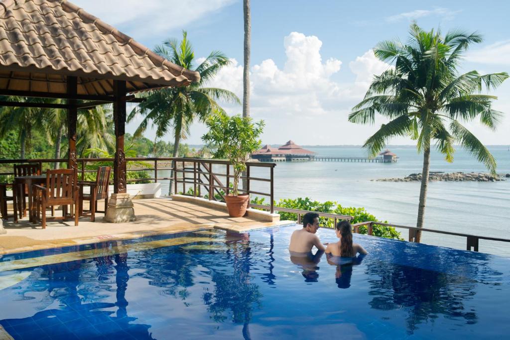 a man and woman sitting in a swimming pool overlooking the ocean at Indra Maya Pool Villas in Lagoi