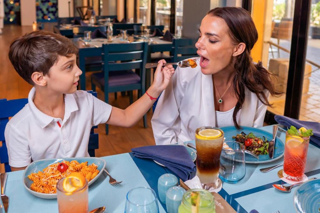 a woman feeding a boy food at a table at Rixos Bab Al Bahr - Ultra All Inclusive in Ras al Khaimah