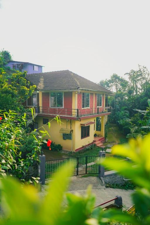 a yellow and red house with a fence and trees at Eshwari Cottage in Madikeri