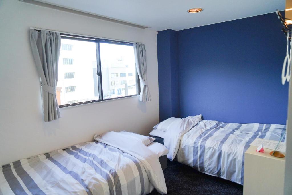 Cette chambre comprend 2 lits dans une chambre dotée de murs bleus et d'une fenêtre. dans l'établissement ゲストハウス CYCLE&STAY, à Tokushima