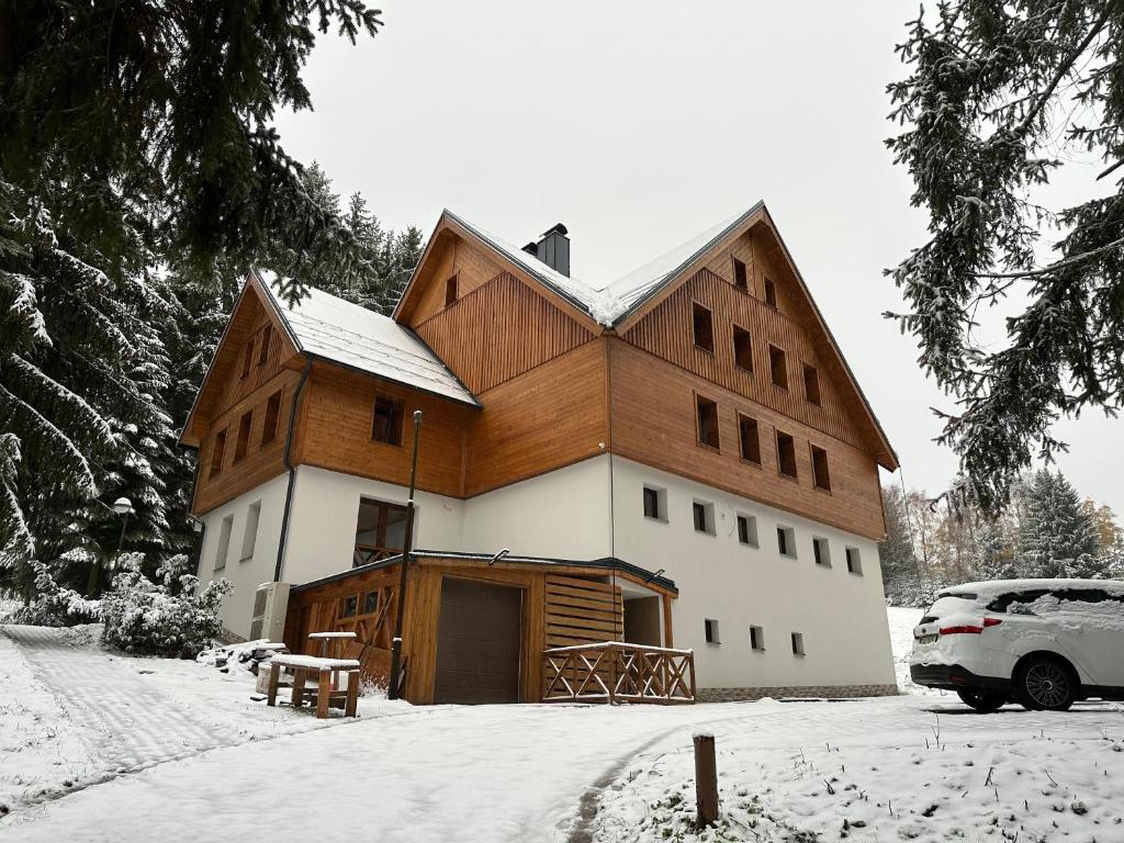 a house with a wooden roof in the snow at Apartmány VESNA in Nova Ves nad Nisou