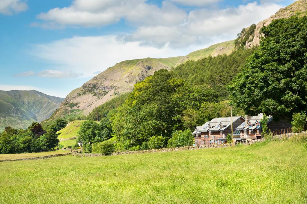 una casa en un campo con montañas en el fondo en The Lodge In The Vale en Thirlmere