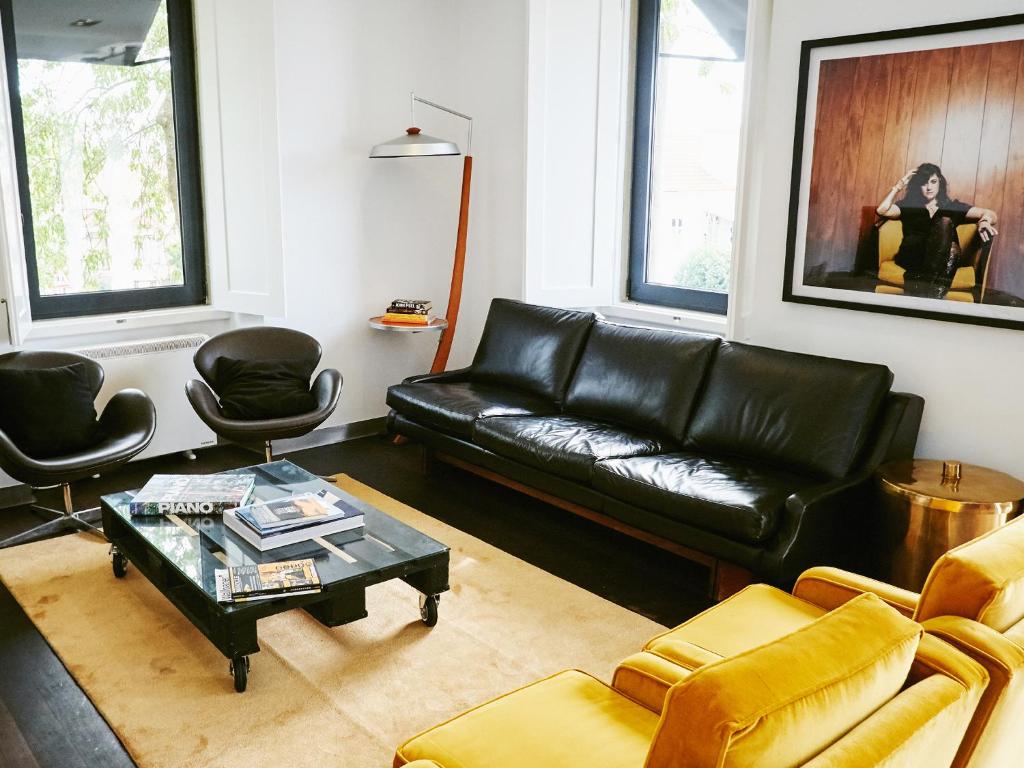 una sala de estar con un sofá de cuero negro y sillas en Bonvalot Guest House, en Paço de Arcos