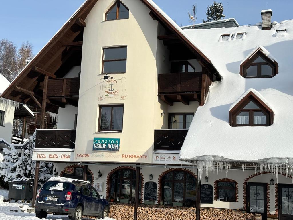 una casa nella neve con un'auto parcheggiata di fronte di Penzion Verde Rosa a Harrachov