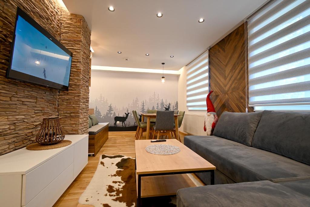 een woonkamer met een bank en een tv aan een bakstenen muur bij Grand Apartment Lučić in Jahorina