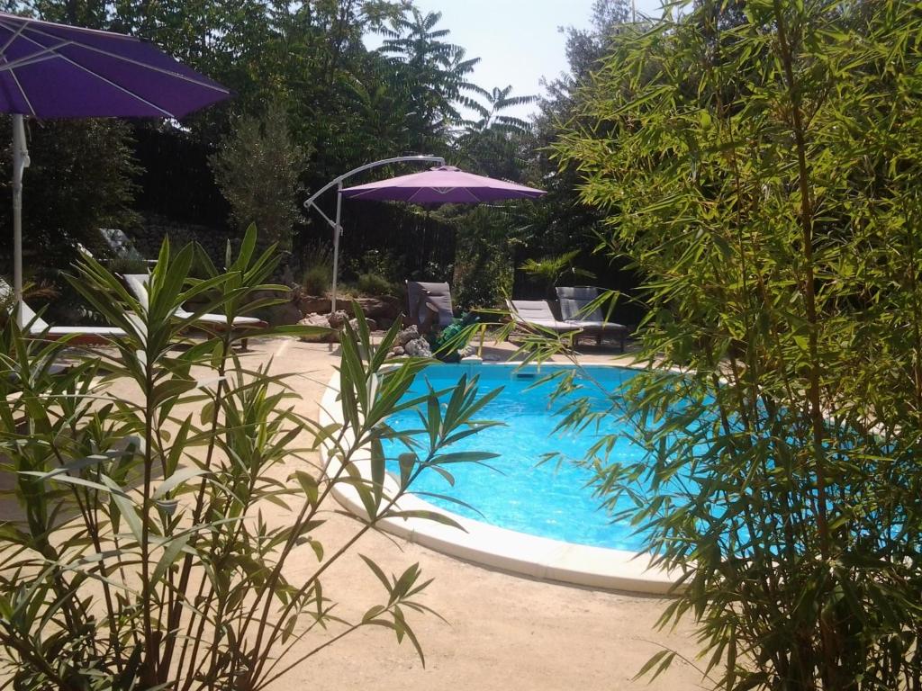 a swimming pool with a purple umbrella and trees at Gîtes Les 3 Cigales in Vallon-Pont-dʼArc