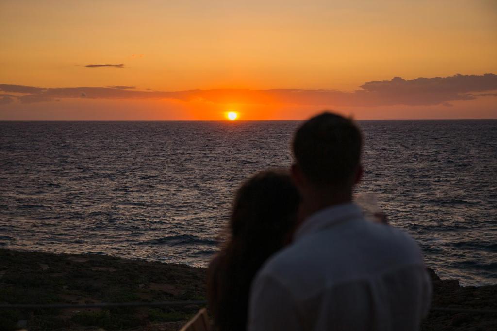 a man and a woman watching the sunset on the beach at Hostal La Torre Ibiza Cap Negret in San Antonio