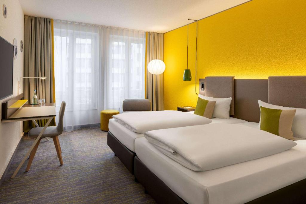 a hotel room with two beds and a desk at Vienna House Easy by Wyndham Leipzig in Leipzig