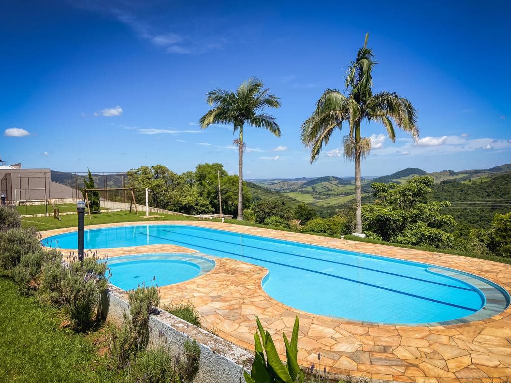 a swimming pool with palm trees and mountains in the background at Lindo apto com lazer completo em Aguas de Lindoia in Águas de Lindóia