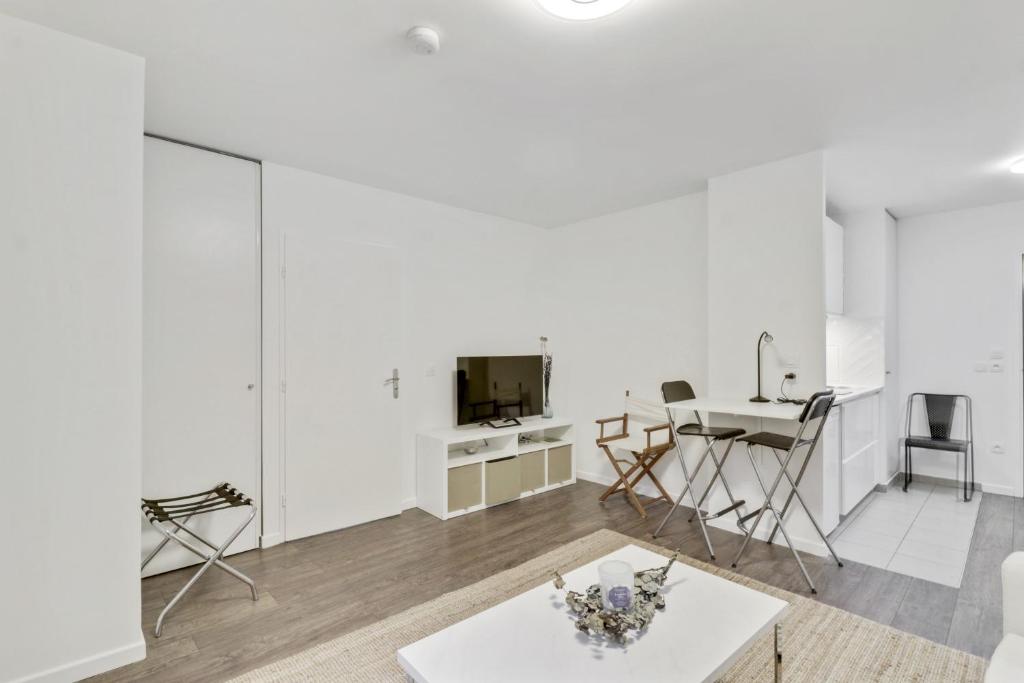 ein weißes Wohnzimmer mit einem Tisch und einem TV in der Unterkunft Chic studio Appartment in Rosny-sous-Bois