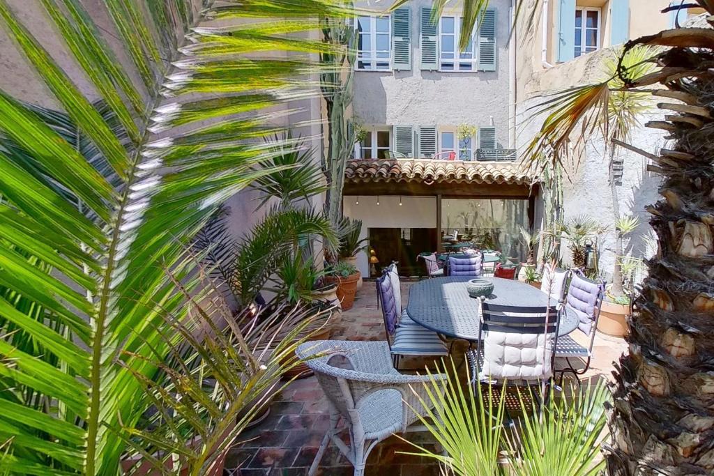 un patio con una mesa, sillas y una palmera en La Maison du Prince en Grimaud