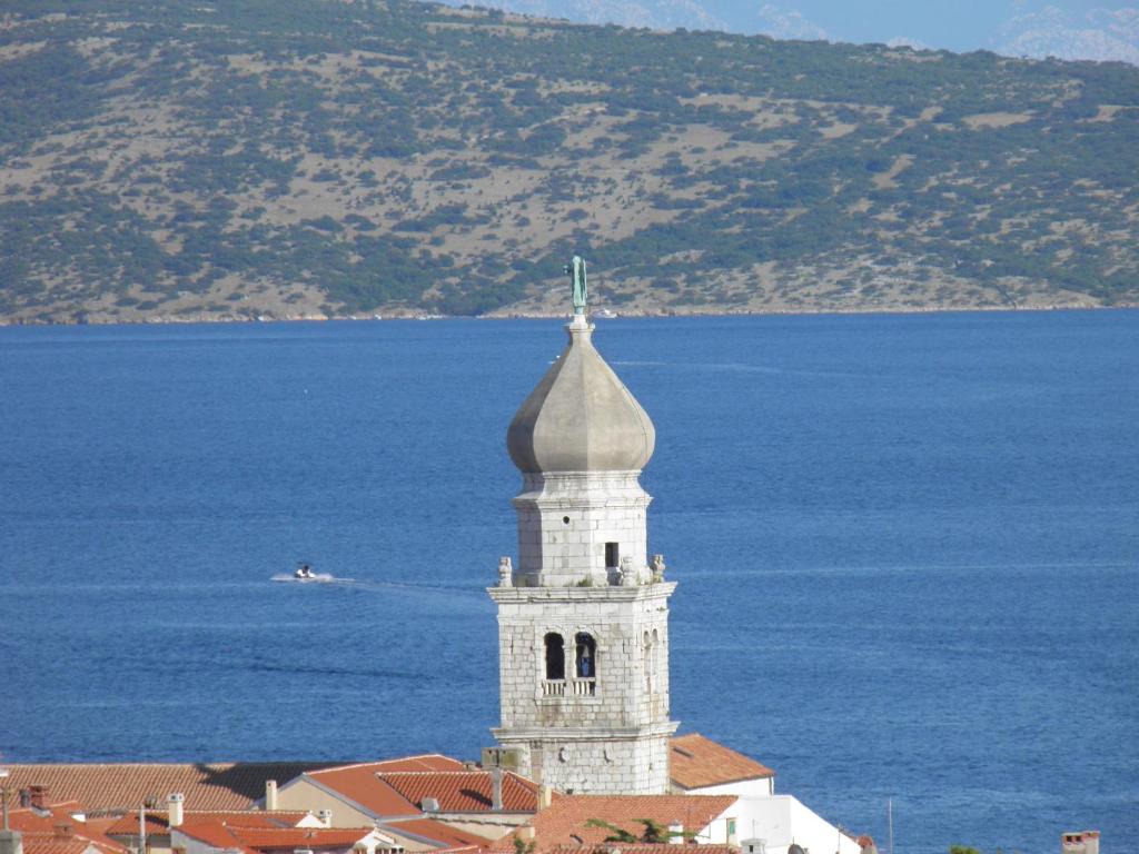 a white tower with a cross on top of a building near the water at Studio Apartments Maslinik in Krk