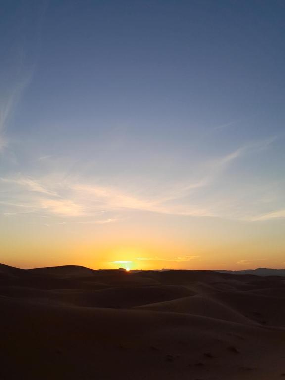a sunset in the desert with the sun setting at Dunes luxury camp in Merzouga