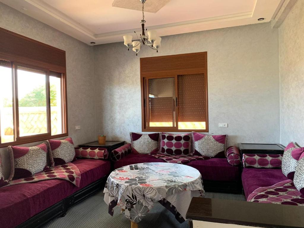 una sala de estar con sofás morados y una mesa. en Villa avec piscine à louer aux environs de Birjdid 46km km de Casablanca route d'El Jadida, en Bir Jedíd Saint-Hubert