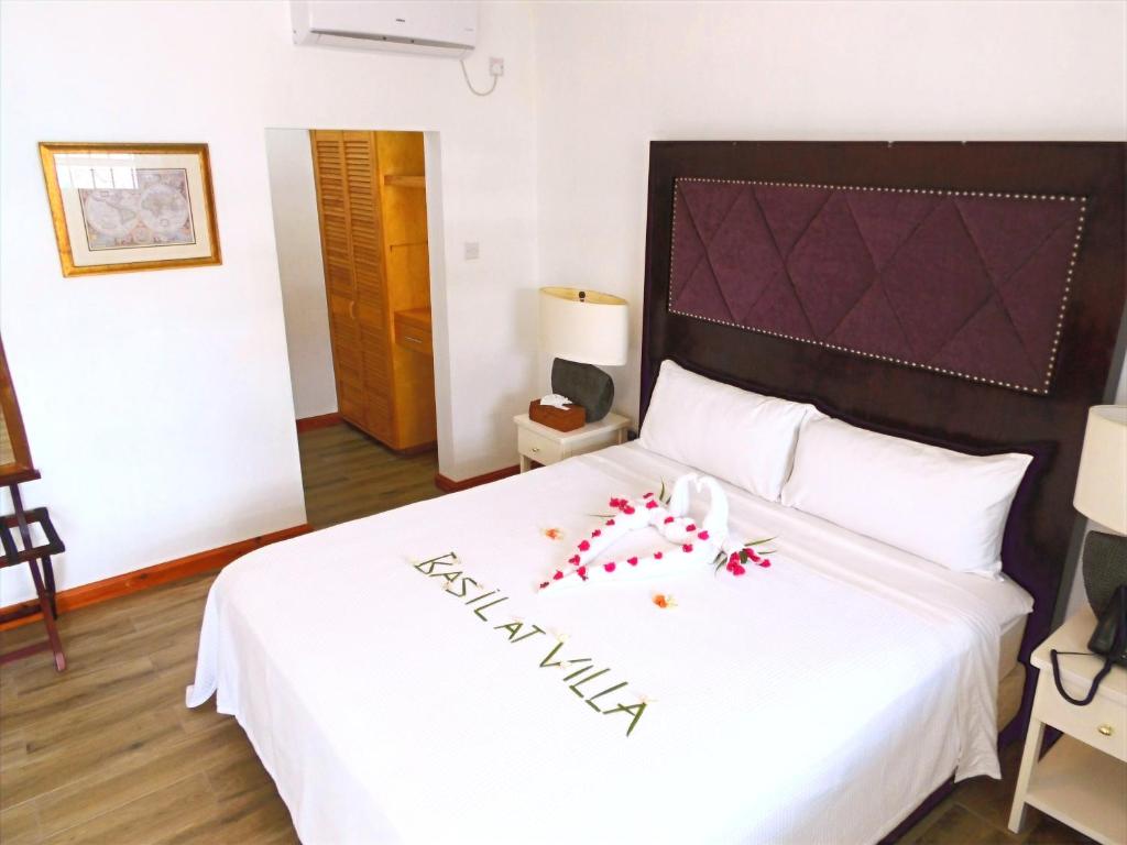 Un dormitorio con una cama con sábanas blancas y flores rojas. en Basil At Villa, en Arnos Vale