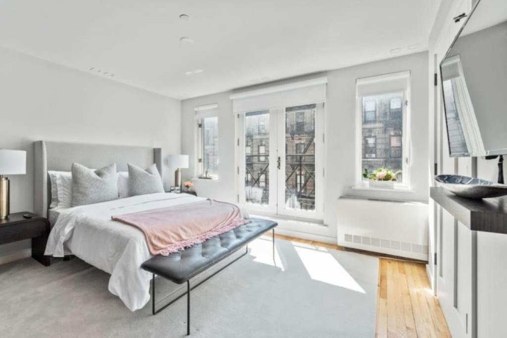 ein weißes Schlafzimmer mit einem Bett und Fenstern in der Unterkunft Luxe Studio with Charming Juliet Balcony in New York