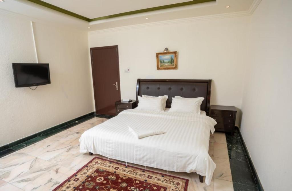 a bedroom with a large white bed with a flat screen tv at Delmon Hotel Suites in Jeddah