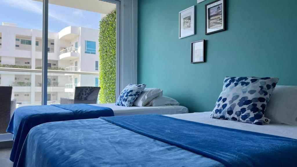2 camas en una habitación con paredes azules y ventana en Cerca al Hotel Americas Ctgna Spiaggia Morros Piscina playa, en Cartagena de Indias
