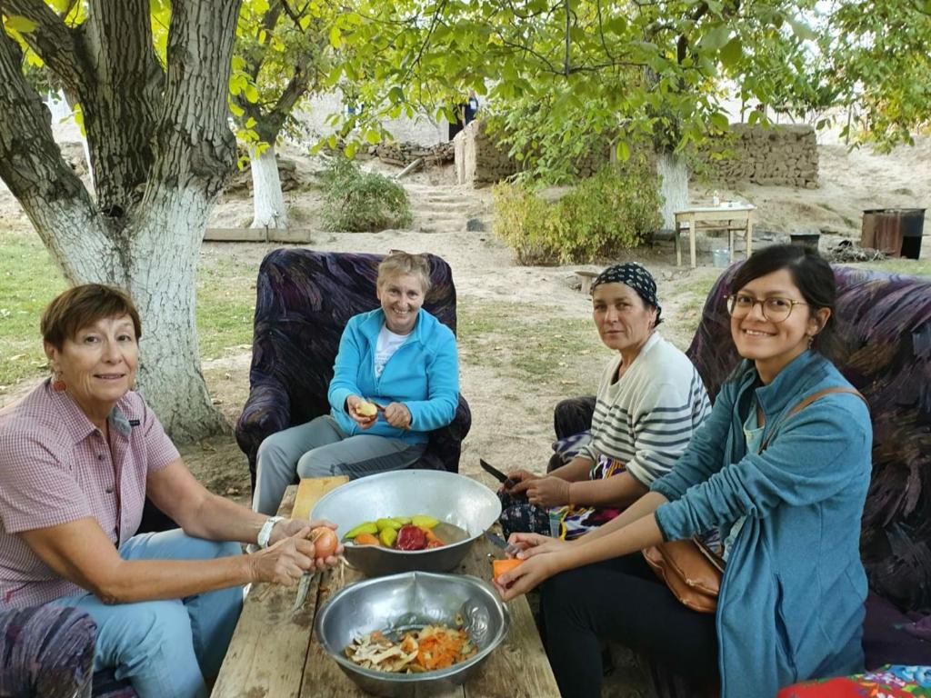 a group of women sitting around a table with a bowl of food at Kuldosh`s homestay in Majrum village in Madzherum