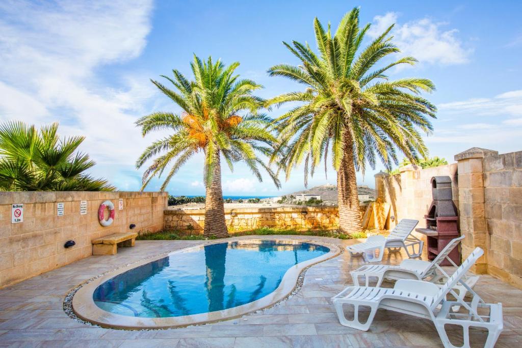 a pool with two palm trees and two chairs at 5 Bedroom Farmhouse with Private Pool & Views in Għarb