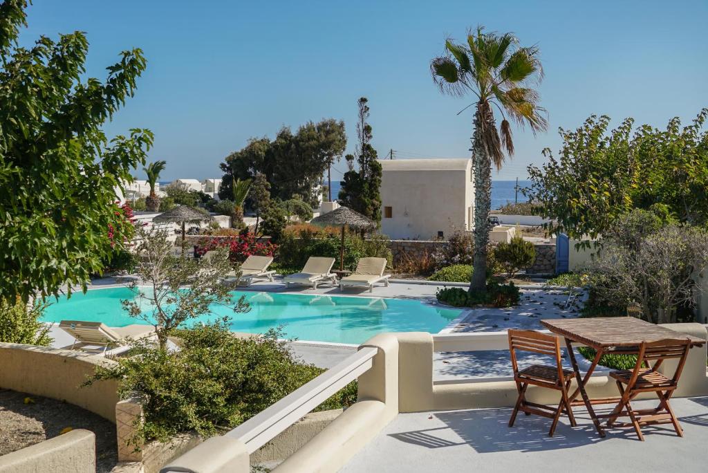 een resort met een zwembad met stoelen en een tafel bij Theros Houses Santorini in Kamari
