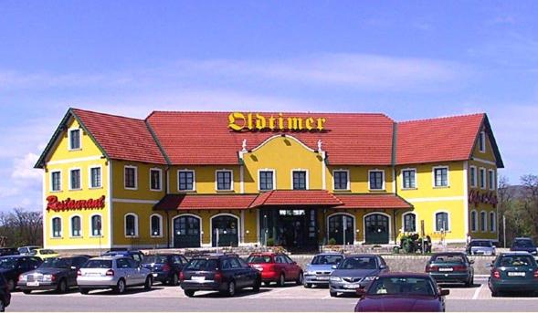 un edificio amarillo con techo rojo y coches aparcados fuera en Oldtimer Motorhotel Guntramsdorf, en Guntramsdorf