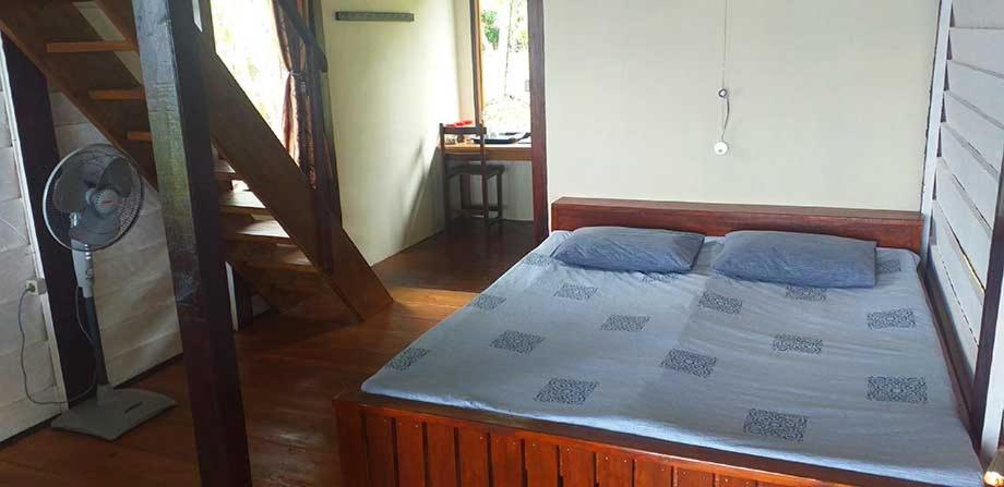 a bedroom with a bed with blue pillows and a fan at Bogani-Cottages in Beniha