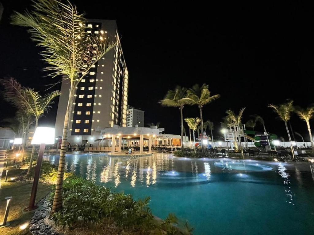 uma piscina à noite com um edifício e palmeiras em Apartamento em Salinas Exclusive Resort em Salinópolis