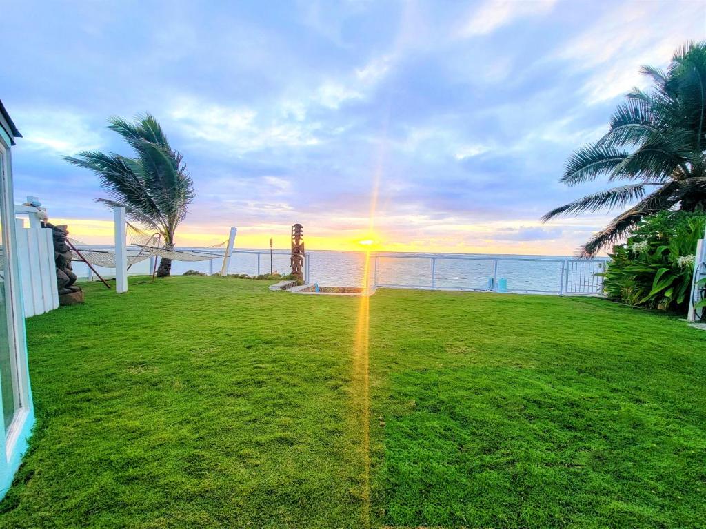a lawn with a view of the ocean at sunset at Corner Luxury Ethereal Hawaii Beachfront Estate for Monthly Rental with Private Beach & 3 Beachfront Jacuzzis & Snorkeling Reef & Jurassic Park Film Site in Punaluu