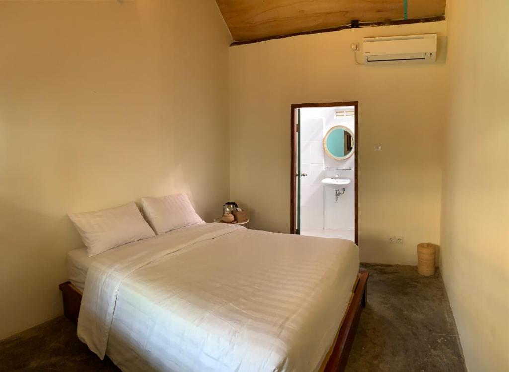 Roots Hotel Trawangan في Pawenang: غرفة نوم بسرير ابيض ومغسلة
