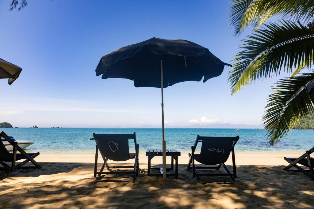 zwei Stühle und ein Tisch unter einem Sonnenschirm am Strand in der Unterkunft Barefoot Project formerly Baan Klong Kleng in Ko Phayam