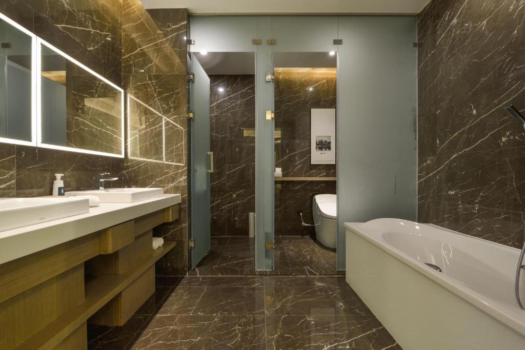 een badkamer met 2 wastafels, een bad en een toilet bij Atour Hotel Railway Station Dalian in Dalian
