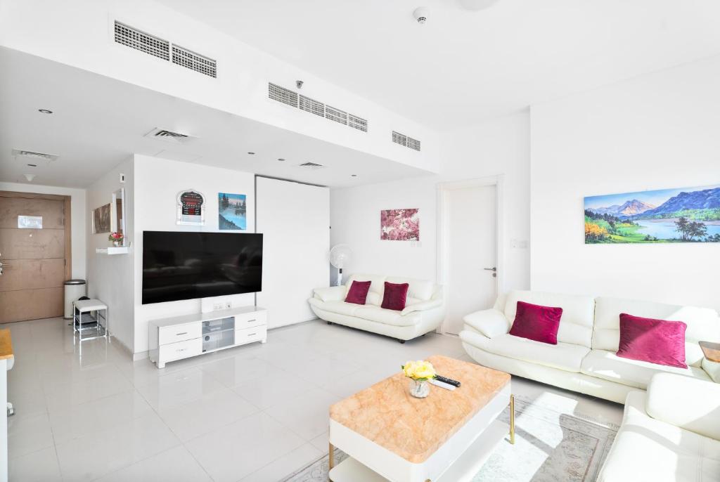 uma sala de estar com mobiliário branco e uma televisão de ecrã plano em Nasma Luxury Stays - Serenity by the Sea 1BR Apartment With Beach Views em Abu Dhabi