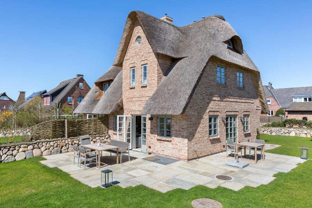 a house with a thatched roof with a table and chairs at Hues Kjerte in Wenningstedt