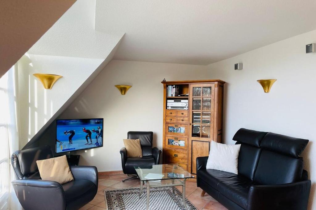 uma sala de estar com cadeiras de couro preto e uma televisão em Landhaus Normannenweg App 4D em Wenningstedt