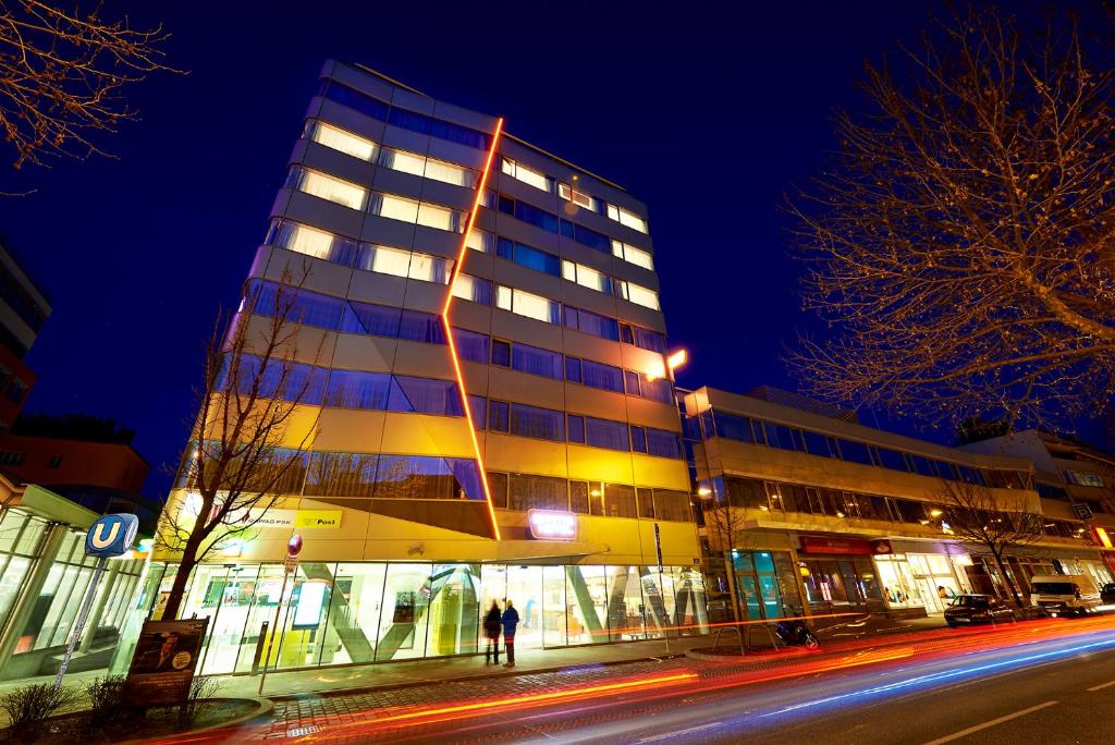 un edificio alto por la noche con gente de pie delante de él en Simm's Hotel - cityhotel next to Metro U3 en Viena