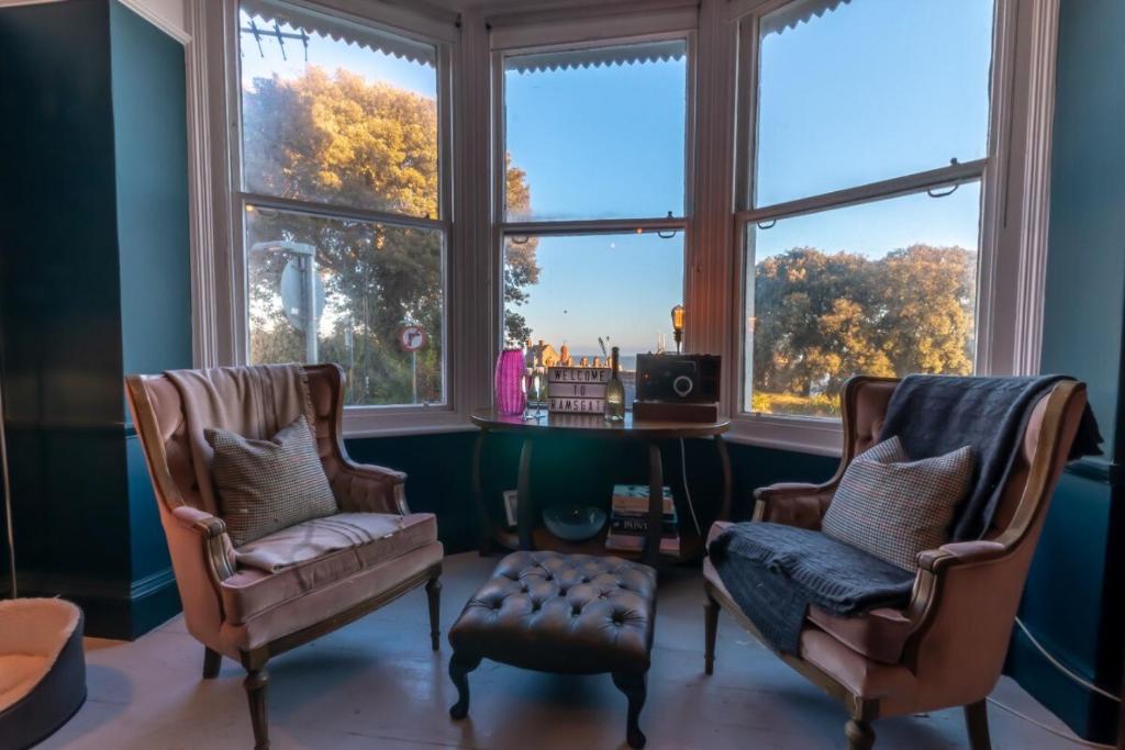 ein Wohnzimmer mit 2 Stühlen, einem Schreibtisch und Fenstern in der Unterkunft Victorian Apartment With Sea Views By Adliv Host in Ramsgate