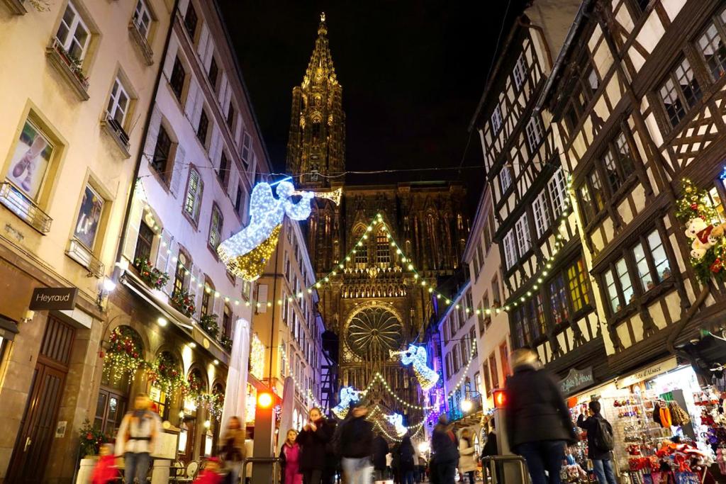 a group of people walking down a street with christmas lights at CHAMBRES DANS CHARMANTE MAISON ALSACIENNE in Herrlisheim