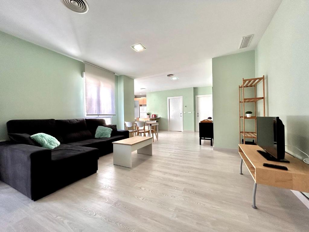 ein Wohnzimmer mit einem schwarzen Sofa und einem TV in der Unterkunft Barrio San Miguel Más que apartamentos in Murcia