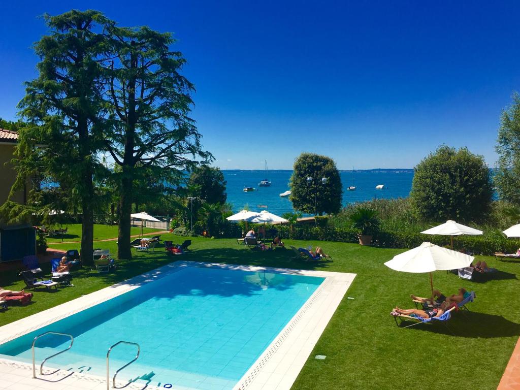 a large swimming pool with people sitting on the grass at Hotel Campagnola in Bardolino