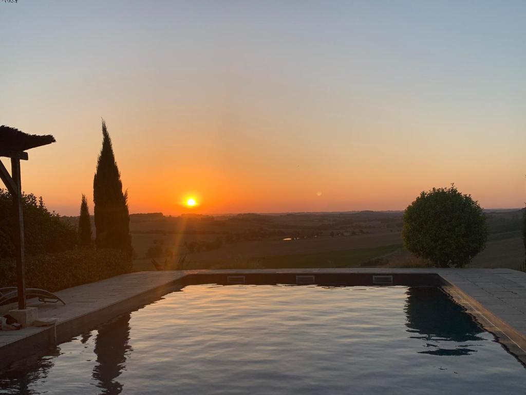 a swimming pool with the sunset in the background at Les 5 terrasses et sa piscine privée in La Sauvetat