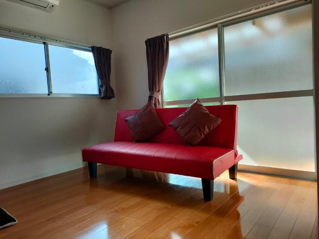 Sofá rojo sentado en una habitación con ventanas en 佐世保　貸切小さな一軒家　GUEST HOUSE　楽楽 Luck-Luck en Sasebo