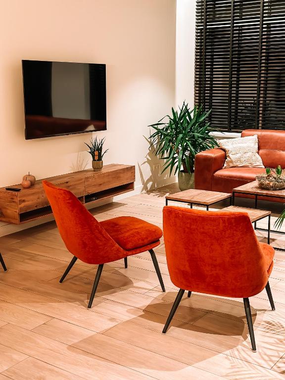 a living room with orange chairs and a tv at Vakantiehuis Maison Madeleine centrum Ieper in Ieper