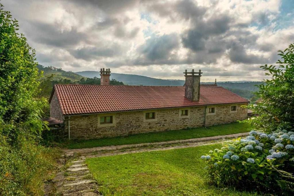 een stenen huis met een rood dak op een heuvel bij Casa Vilaverde Turismo Rural in Coristanco