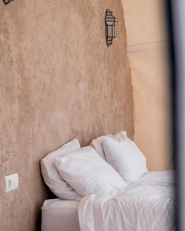 a bed with white sheets and a light on the wall at Emeraude Camp Agafay in El Karia