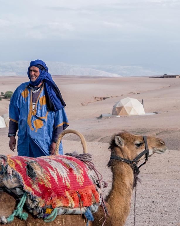 a man standing next to a camel in the desert at Emeraude Camp Agafay in El Karia