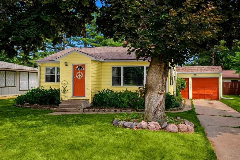 uma casa amarela com uma porta vermelha e uma árvore em French Island Whot Tub, Kayak, Lake View, Ev em La Crosse