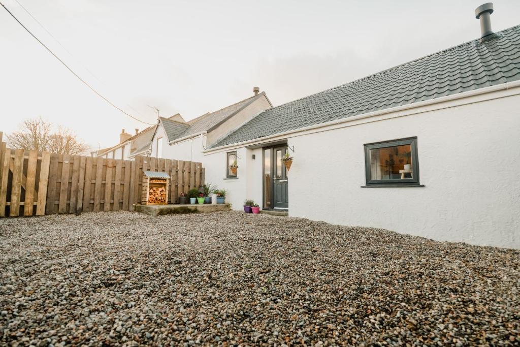 a white house with a fence and a gravel driveway at The Cow Shed at Pencraig in Holyhead